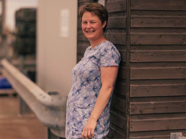 Gill when she was pregnant, wearing a flowery summer dress and standing next to a wooden-clad wall